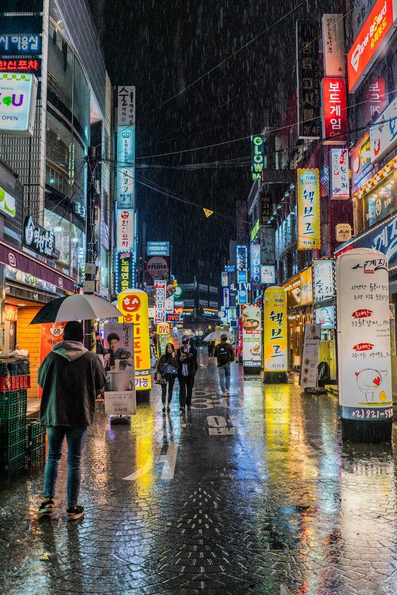 Colorful neon-lit street in Seoul, South Korea showing bustling nightlife with reflections on wet pavement.