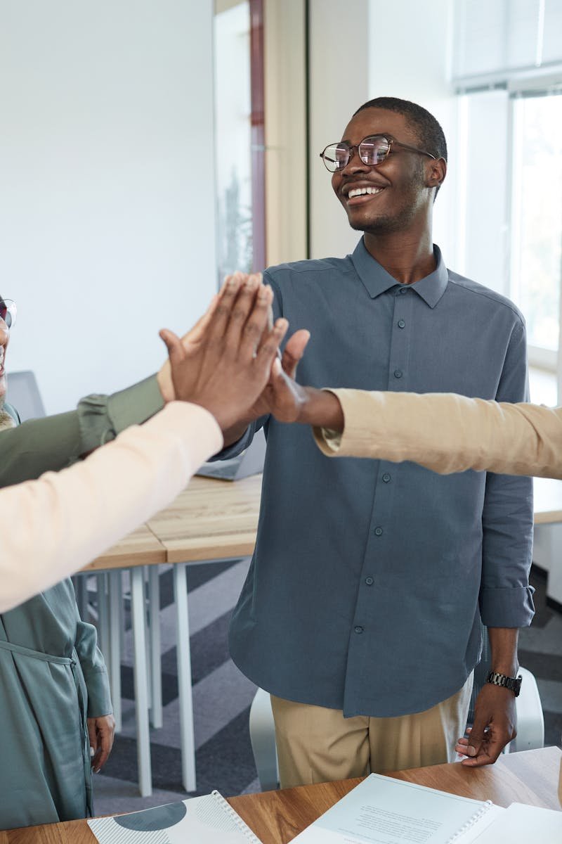 A joyful group of diverse colleagues high-fiving each other in an office, symbolizing teamwork and collaboration.